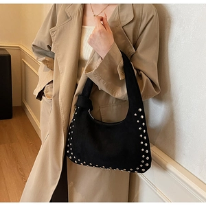 Detail of black suede shoulder bag with silver rivets styled on a khaki trench coat