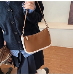 Detail of brown leather shoulder bag with white faux fur trim and gold zipper