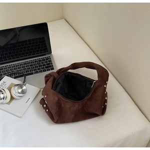 Detail of brown suede tote bag with silver studs and knotted handle next to a laptop