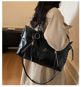 Detail of black leather tote bag featuring metal zipper tassels and adjustable shoulder strap