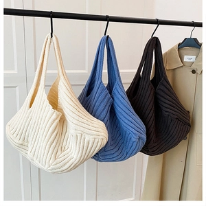 Large striped knit tote bag in off-white and blue hanging on a minimalist rack