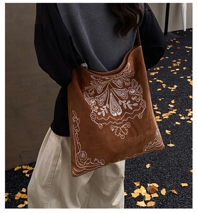 Close-up of white floral embroidery on dark brown suede tote bag in autumn setting