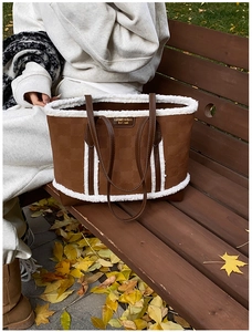 Detail of a brown tote bag with white faux shearling trim on a wooden bench outdoors