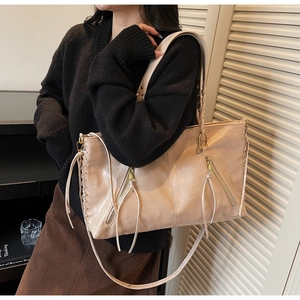 Detail of light brown tote bag featuring woven stitching and decorative metal zipper