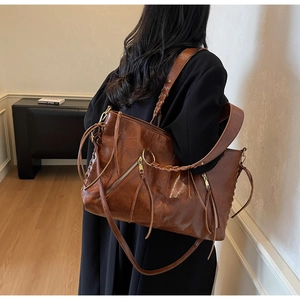Macro detail of brown leather tote bag showing woven handles and long tassel zipper
