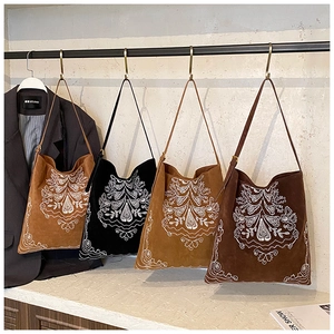 Detailed embroidery on four suede tote bags in various colors on a display rack
