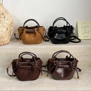 Minimalist bucket bags in yellow, black, and brown leather displayed on marble steps