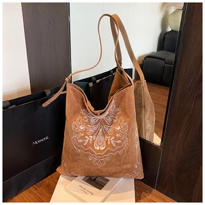 Detailed close-up of bohemian white embroidery on vintage brown suede tote bag