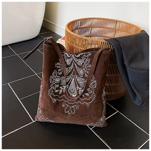 Close-up of vintage brown suede tote bag with white floral embroidery in a home setting