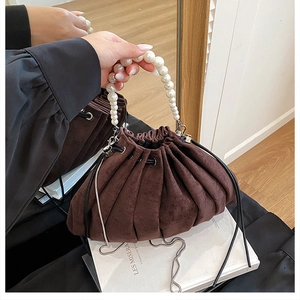 Détail du sac seau en daim avec poignée en perles et design plissé en nuage