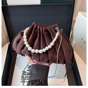 Détail du sac seau en daim marron foncé avec design plissé et poignée élégante en perles