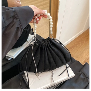 Détail du sac seau plissé noir avec poignée en perles et chaîne en métal sur miroir