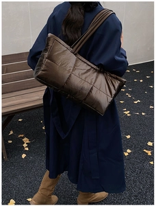 Brown down puffer tote bag shown on a model in a fall park setting with ginkgo leaves