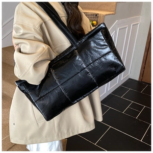 Close-up of black glossy quilted puffer tote bag shown on model for daily lifestyle use