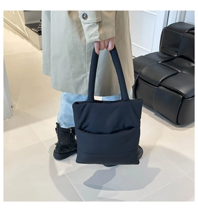 Quilted black tote bag with long handles shown in a minimalist interior setting
