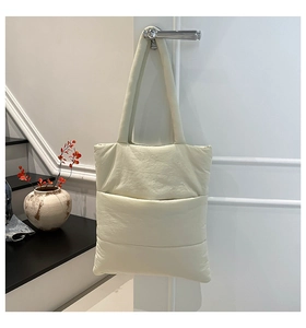 Detail of cream white quilted tote bag featuring soft puffer texture and wide shoulder strap