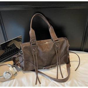 Detail of dark brown leather tote bag with boho tassels and cross-strap stitching accents