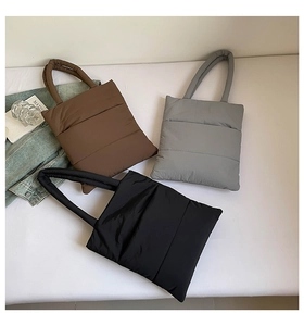 Three quilted tote bags in black, coffee, and gray with soft puffy texture on a beige surface