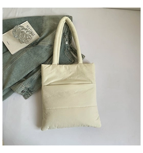 Close-up of quilted cream tote bag with horizontal stitching on a cozy bed background