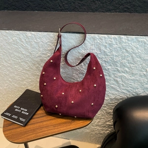 Dettaglio borsa hobo in camoscio bordeaux con borchie dorate su un tavolo di legno
