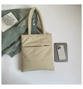 Flat lay of khaki quilted puffer tote bag with lifestyle accessories on white surface