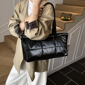 Quilted black puffer tote bag in glossy finish shown as a large shoulder bag on a model