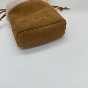 Dettaglio borsa a secchiello in camoscio marrone con bordo in peluche bianco e ricamo