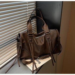 Détail du sac cabas marron vintage avec pompons décoratifs et poignée lacée sur un rebord