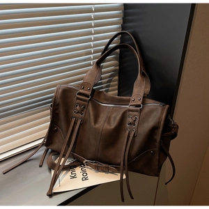 Détail d'un grand sac cabas marron foncé en simili cuir avec œillets et longues franges