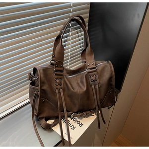 Détails d'un sac Boston marron foncé avec clous en métal, franges et texture PU souple