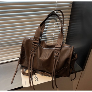 Détail du sac cabas en cuir marron foncé avec lanières croisées et pompon décoratif