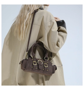 Detail of dark brown suede crossbody bag with gold buckles and adjustable shoulder strap