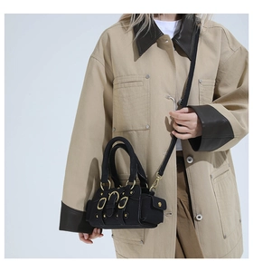 Detail view of black utility crossbody bag with three golden buckle pockets and handles