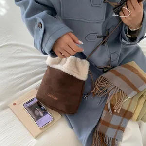 Dettaglio borsa a secchiello in camoscio marrone con bordo in pelliccia bianca e logo