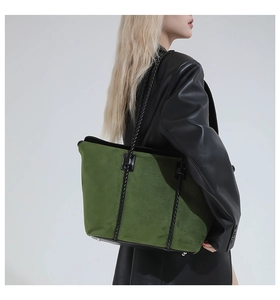 Detail of green suede tote bag with black woven straps worn by model in leather jacket