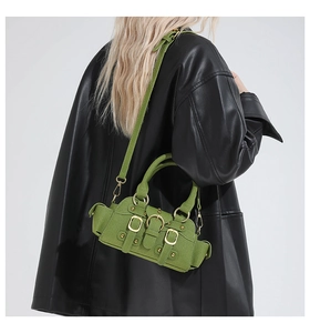 Detail of green mini handbag with gold buckles worn over a black leather jacket