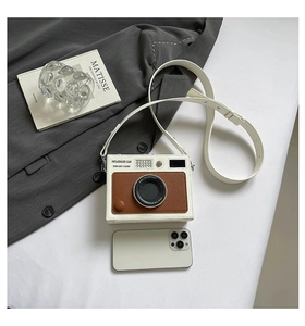 Detail view of a vintage camera-shaped crossbody bag with a smartphone for size reference