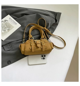 Detail of tan suede mini handbag featuring decorative buckles and metal hardware accents
