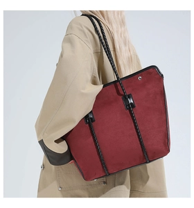 Close-up of a burgundy suede tote bag with black woven handles on model shoulder