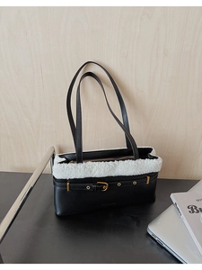 Detail of black PU shoulder bag with white faux fur trim and gold buckle on a desk