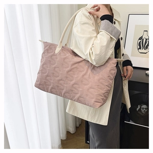 Close-up of pink quilted tote bag featuring embossed S patterns and cream shoulder strap