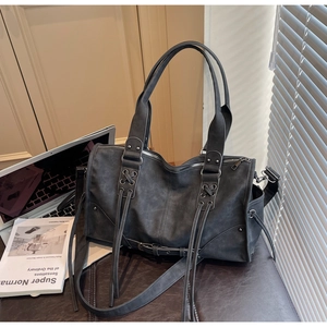 Détail d'un sac polochon rétro gris foncé avec pompons et rivets métalliques