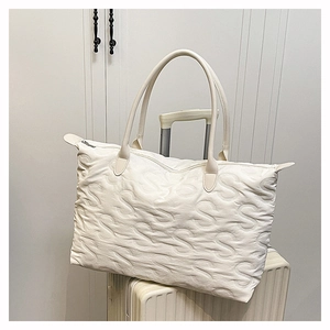 Macro shot of white quilted tote bag with textured S-pattern sitting on a suitcase