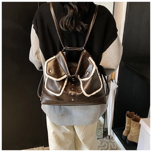 Detail of dark brown tote bag with white faux fur trim and metal studs on a model