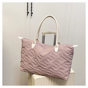 Detail of quilted mauve travel tote with embossed letters on a white suitcase