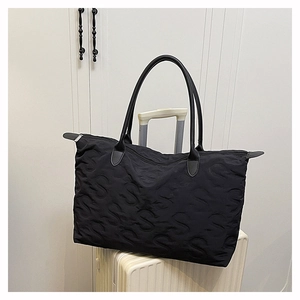 Detail of black quilted tote bag with S-letter pattern resting on a white suitcase