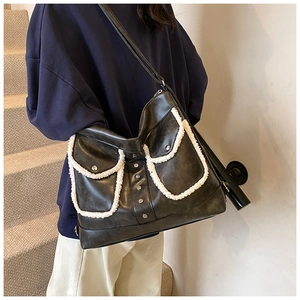 Detail of black leather tote bag featuring white faux shearling trim and silver studs