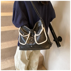 Close-up of black tote bag with white plush trim and silver studs on front pockets