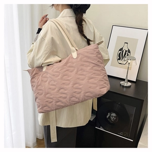 Close-up of pink quilted tote bag with S-letter embossing and white handles on a model
