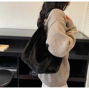 Detail of a large black faux fur hobo bag with a metal buckle strap on a model shoulder